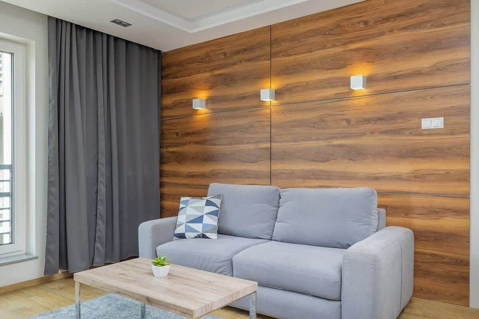 Modern living room with gray couch, wooden accent wall, and warm lighting.