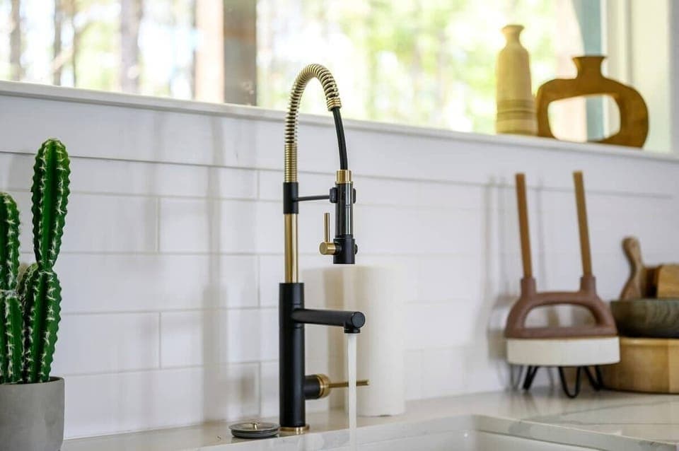 Stylish black and gold kitchen faucet with running water, surrounded by modern decor and natural light.