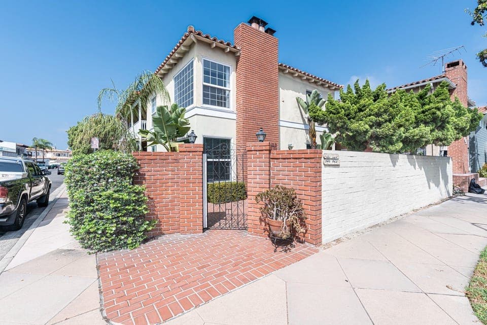 Charming Newport Beach home featuring a classic brick façade, lush landscaping, and a sunny front patio
                