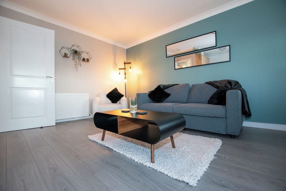 Modern living room with a 55" wall-hung TV, stylish double sofa bed, and boucle armchairs. Wood-pane (1)