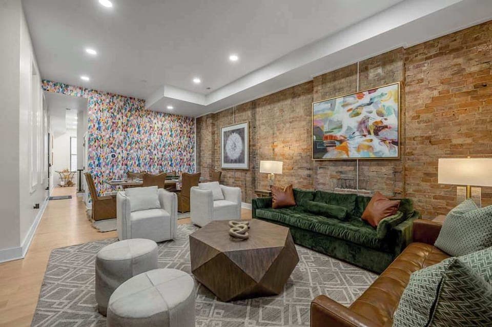 A bright and open living space featuring exposed brick accents, contemporary furnishings, and colorful artwork. The room offers comfortable seating, soft ambient lighting, and a modern yet welcoming vibe, ideal for unwinding or hosting friends.