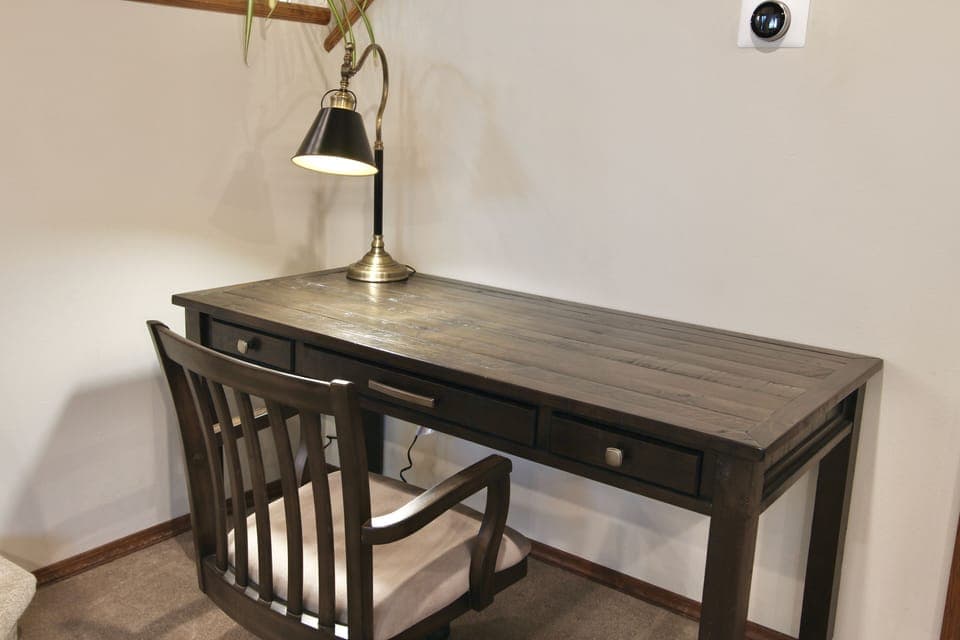 Features a large wooden desk, comfortable chair, laptop stand, and task lamp