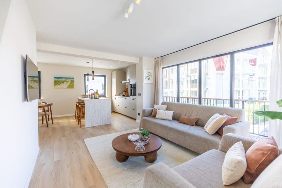 Relax in a spacious, sun-drenched living room with floor-to-ceiling windows, modern furnishings, and access to your private balcony - ideal for a luxury beachside stay.