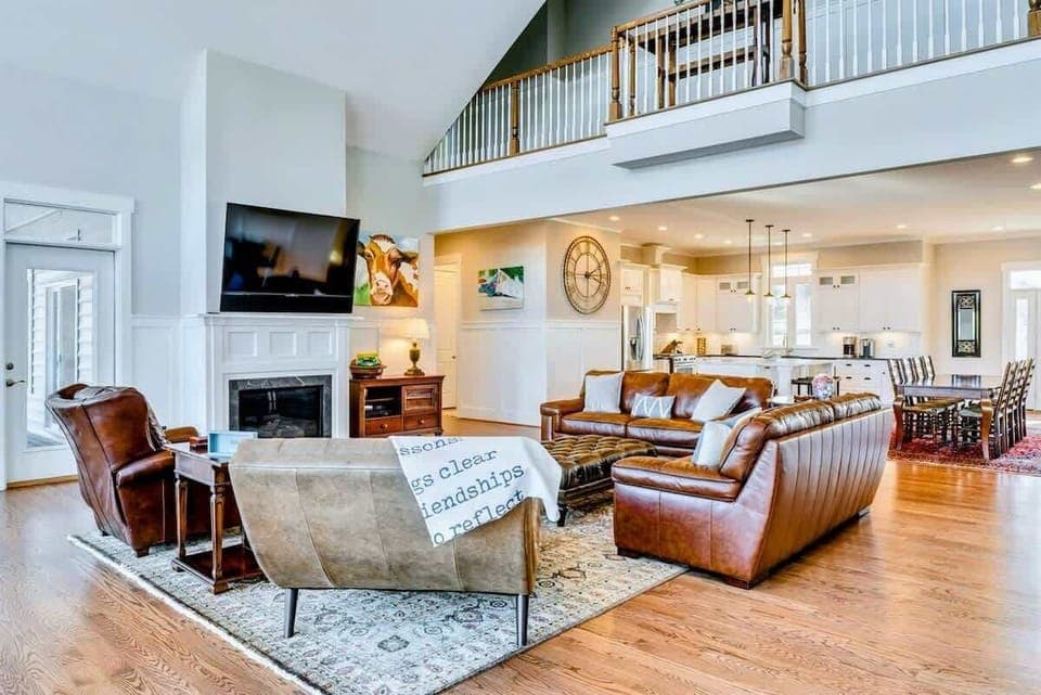 Spacious, open-concept living room with elegant leather seating, a cozy fireplace, and views into the modern kitchen and dining area
