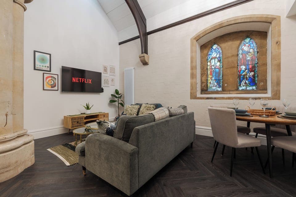 Step into a stunning living and dining area where soaring ceilings and original stained-glass windows bathe a sumptuous couch and elegant dining table in natural light—perfect for cosy evenings in and home-cooked dinners alike.