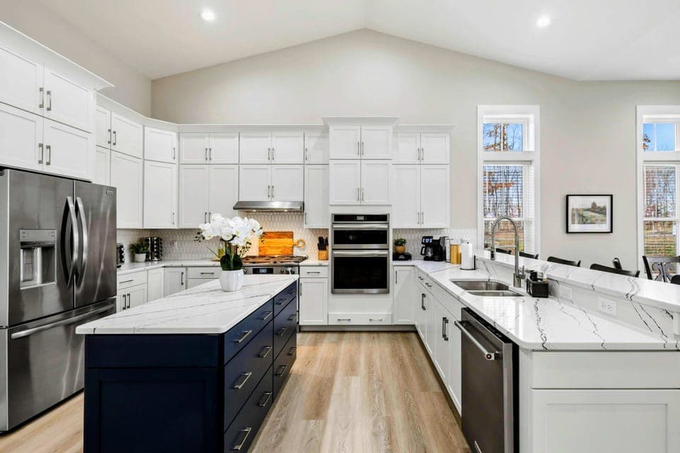 Bright open-concept kitchen and dining area with white cabinets, a navy island, and large windows providing natural light and scenic views.