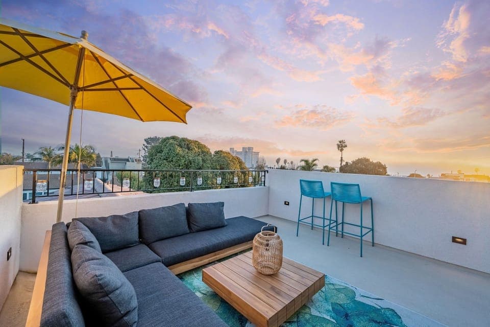 Private rooftop deck extending from the 3rd floor second family room/ game room with beautiful ocean views of Pacific Beach, complete with ample comfortable seating with a sectional and pillows, an umbrella, coffee table, and ambient lighting.