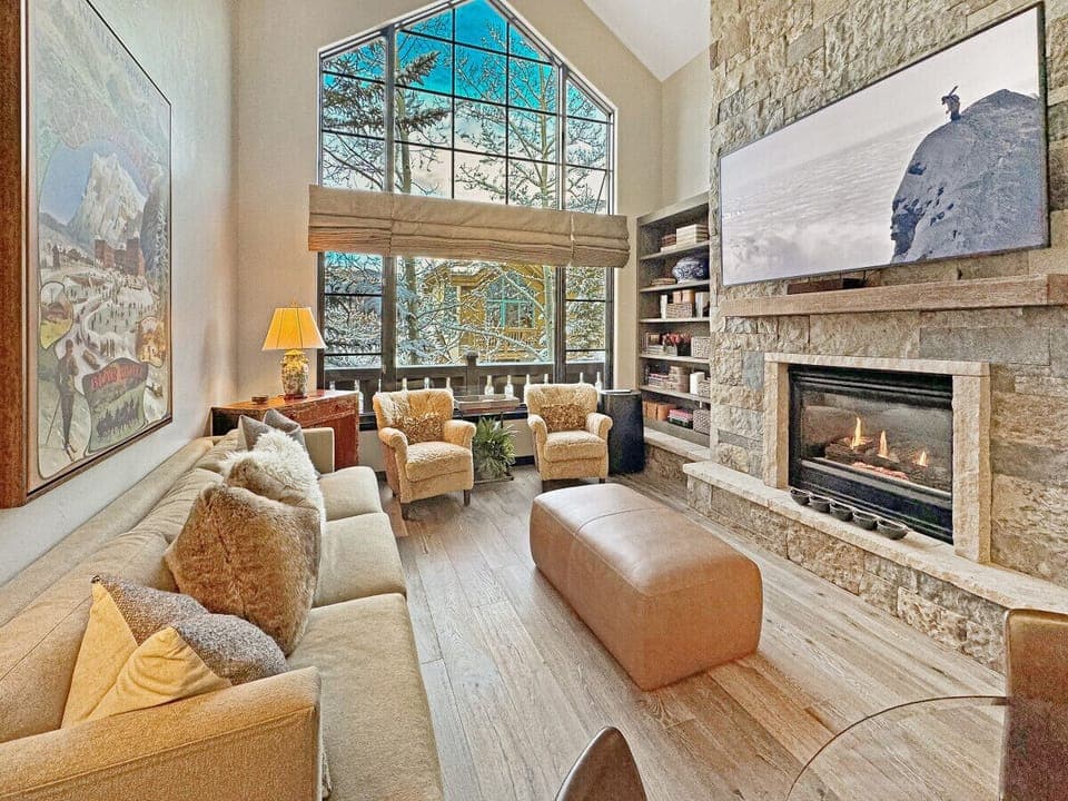 Unwind in the cozy living room with plush seating, a stone fireplace, massive smart TV, and mountain views through soaring windows, perfect après-ski comfort in Arrowhead Village.
