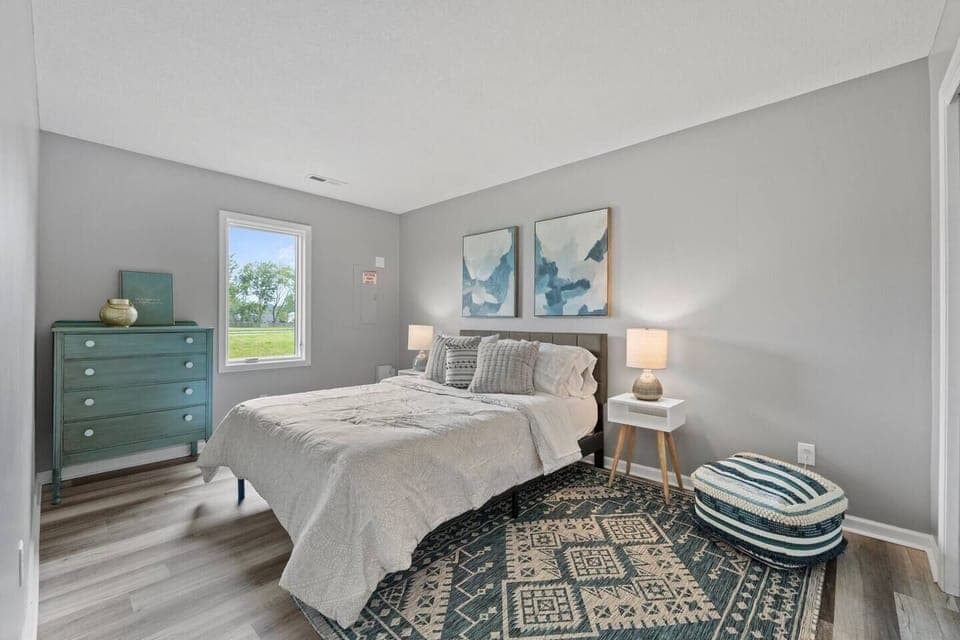 Elegant queen-sized bedroom with a spacious layout and large window, allowing natural light to create a bright and airy atmosphere.
