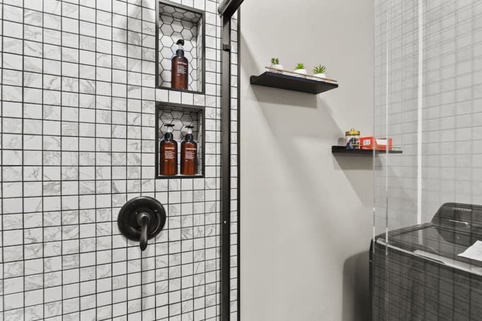 Modern full bathroom featuring a glass-covered shower, elegant walling, a shower heater, and neatly arranged shampoo and body wash—designed for functionality and relaxation with a touch of sophisticated style