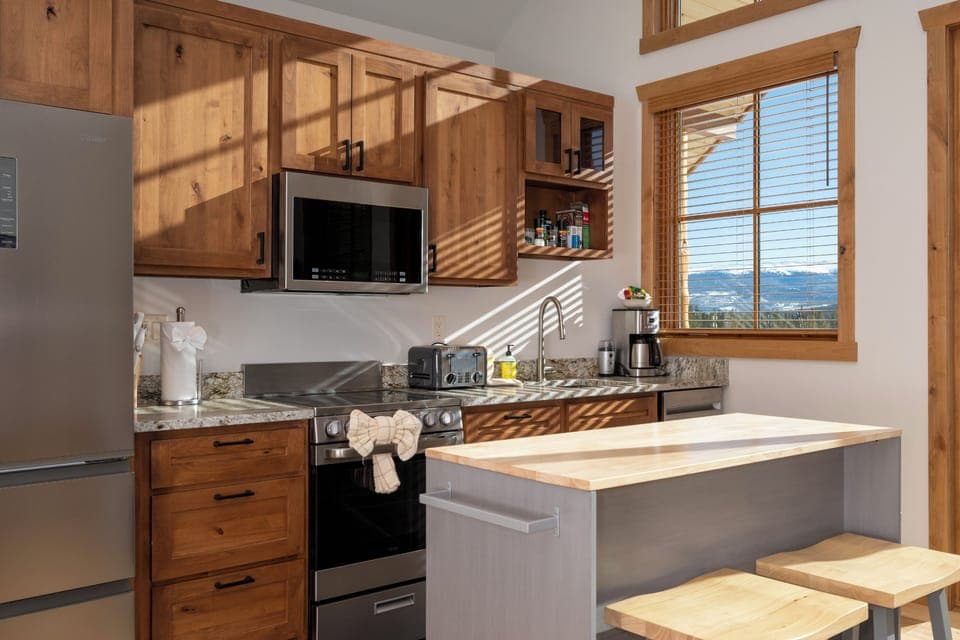 Your fully equipped mountain kitchen blends warm wood cabinetry with modern appliances, bathed in golden light from stunning valley views.