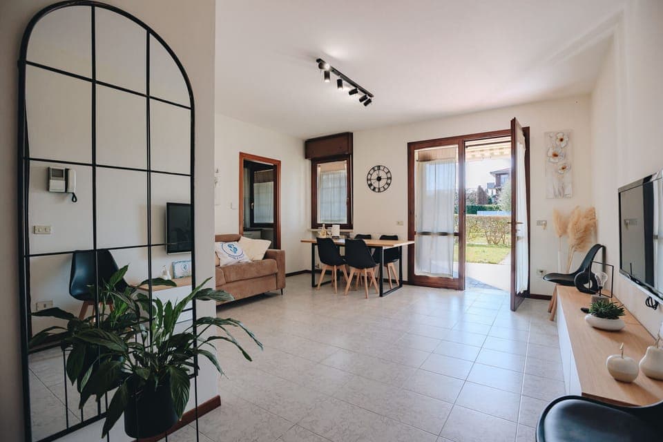 Cozy apartment in Peschiera del Garda with a spacious living room and direct access to a private garden. Furnished in a modern style with natural details, it features a relaxation area with a sofa and flat-screen TV, a dining area, and large windows that make the space bright and airy. Ideal for couples or families who want to stay in a quiet area, just a few minutes from the center and the shores of Lake Garda.