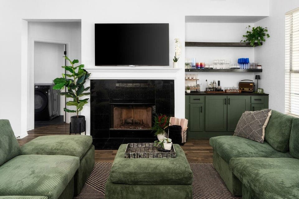 Cozy up in this stylish living room, featuring plush green seating, a warm fireplace, a built-in bar, and a large TV for the perfect blend of comfort and entertainment!