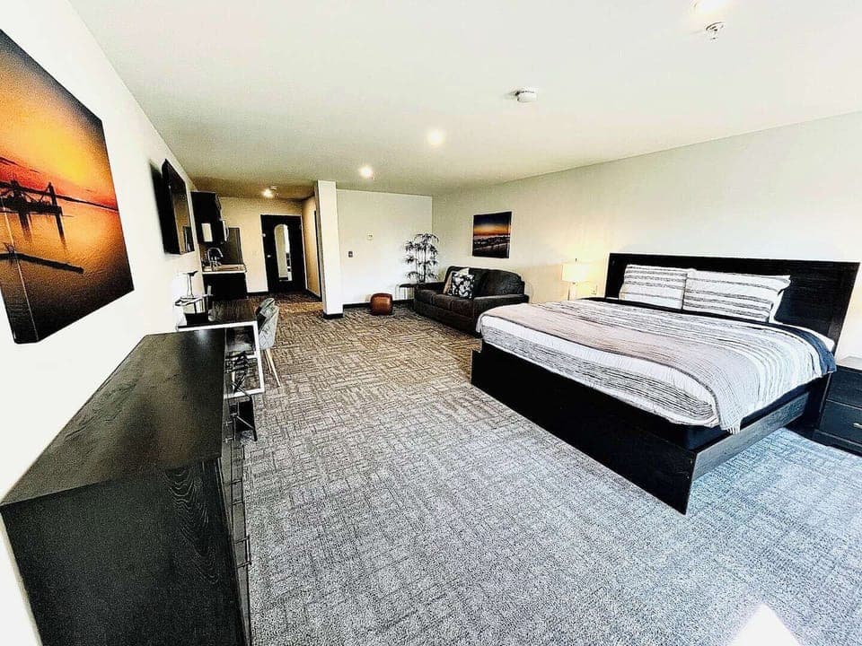 A bright, open room featuring a comfortable bed, work desk, ample storage, and a large TV, perfect for relaxing or working during your stay.