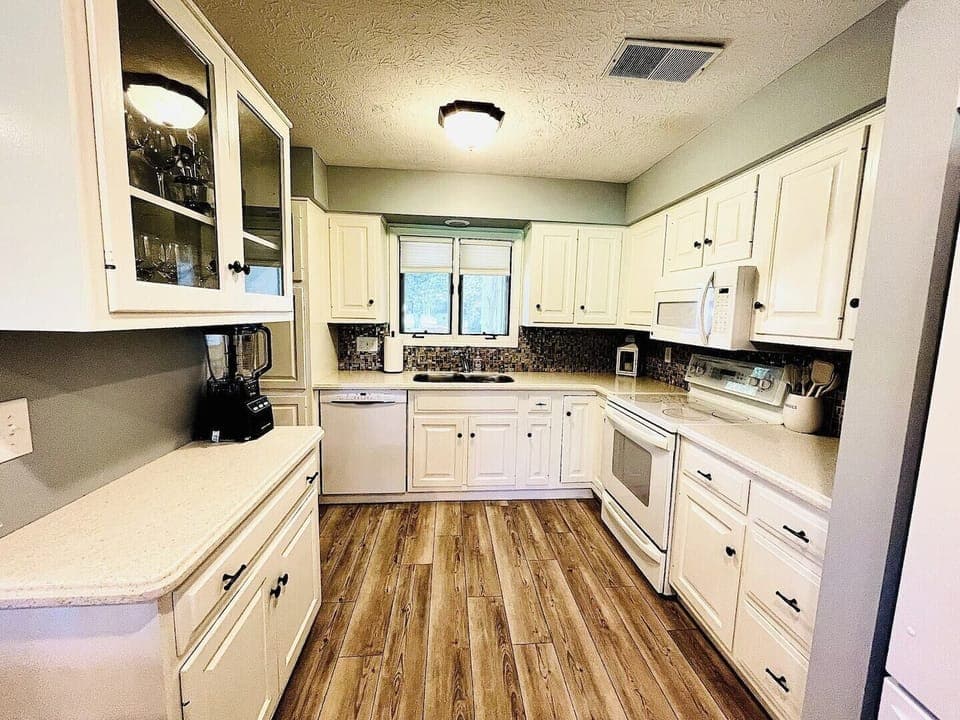 A spacious and bright kitchen with classic white cabinets, modern appliances, and a cozy layout, ideal for preparing family meals.