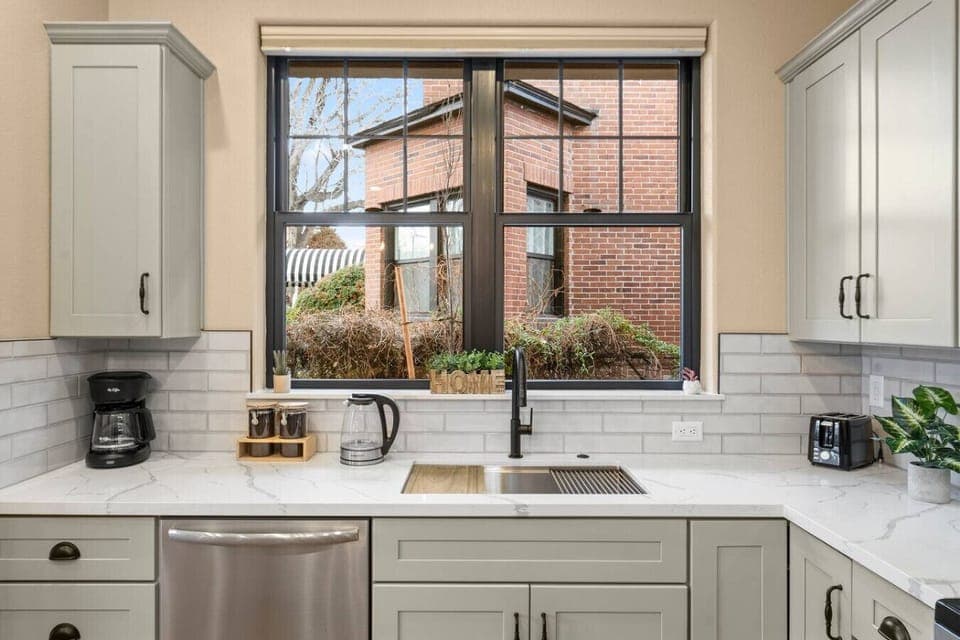 Cook with a view! This bright and modern kitchen features sleek countertops, stainless steel appliances, and a charming window overlooking a quaint brick building.