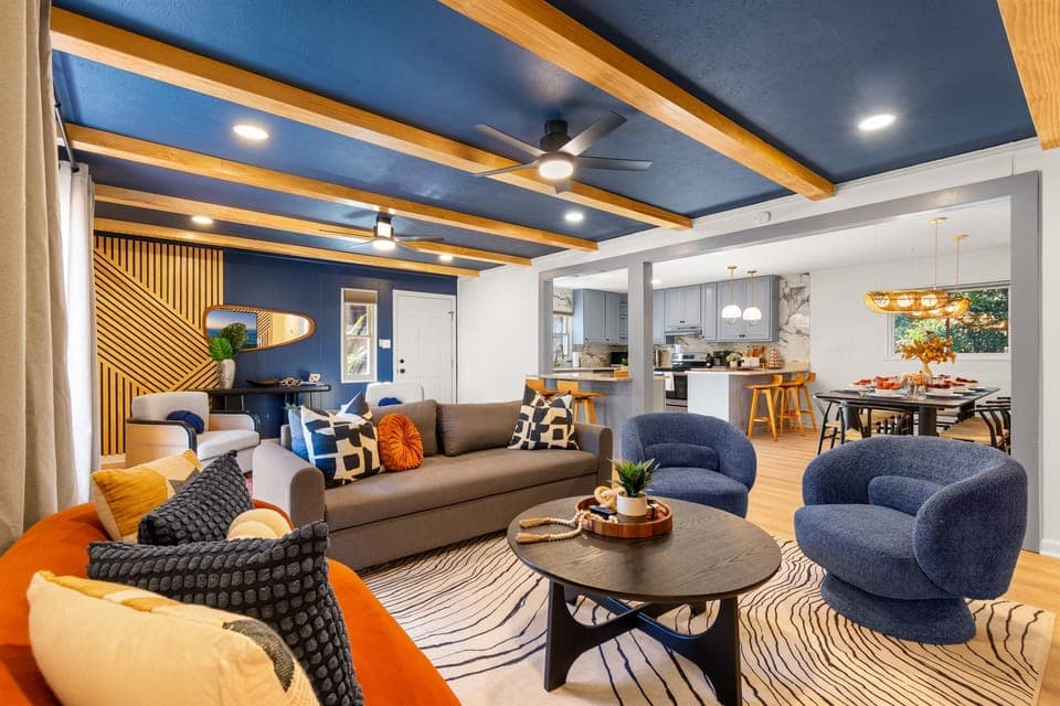 Stylish blue and wood accented ceilings add a touch of elegance to this open-concept living space. Bright and inviting living room with artistic decor and plush furniture.