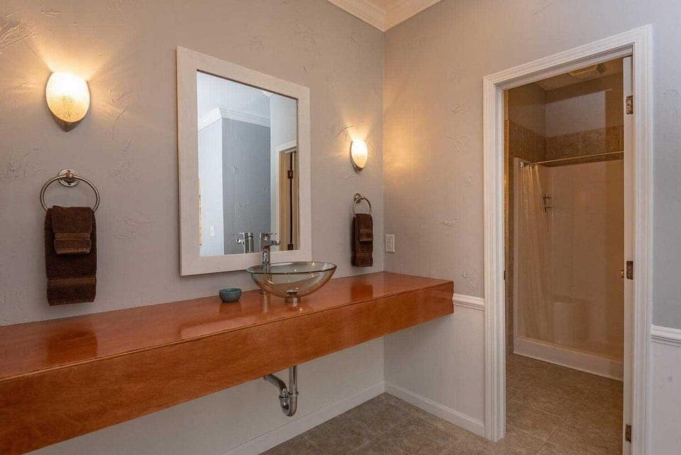 Wall-mounted frosted glass vessel sink rests on a wood floating countertop with matching brown towels.