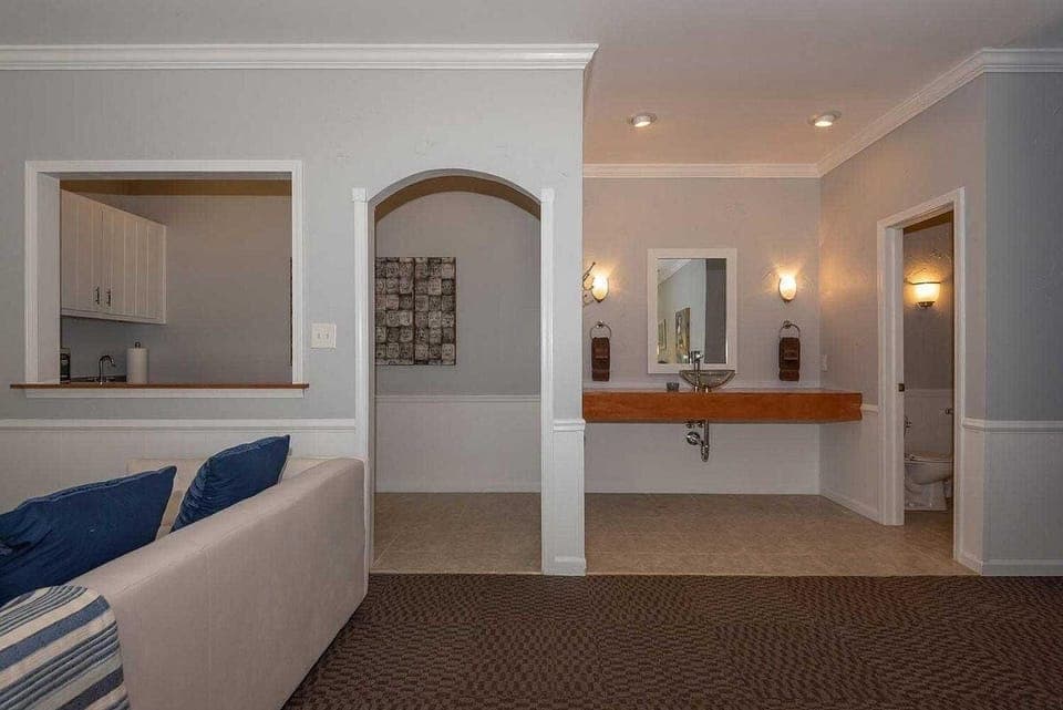 Open archway and pass-through window connect the living area to the kitchenette and bathroom sink with wood countertop.