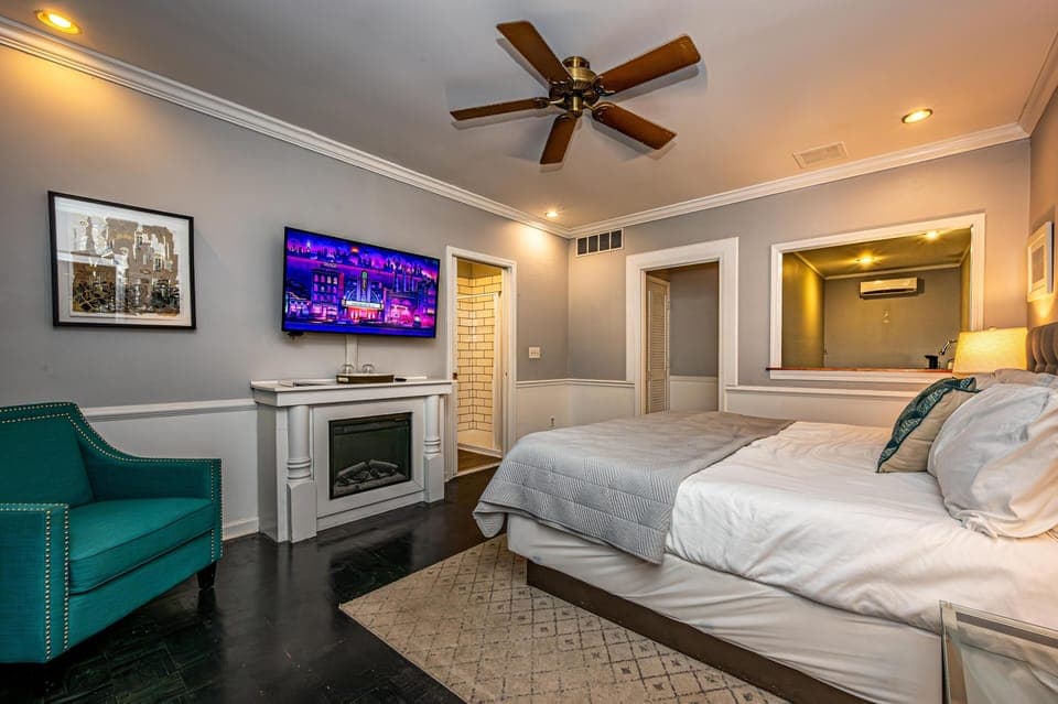 Bedroom featuring a king bed with white linens, a teal armchair, wall-mounted TV, and a ceiling fan.