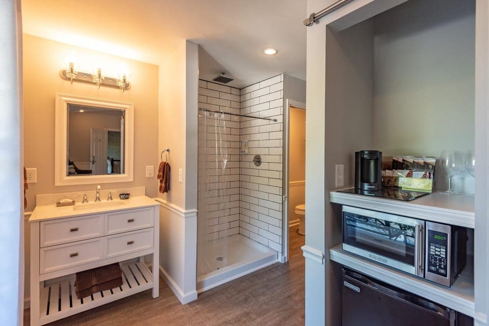 Bathroom vanity with white drawers and silver fixtures sits beside a walk-in shower with subway tile and clear curtain.