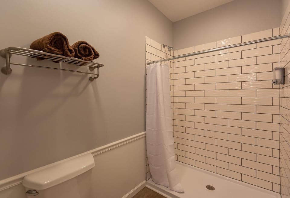 Bathroom features a walk-in shower with white subway tiles, a white curtain, and a metal towel rack.