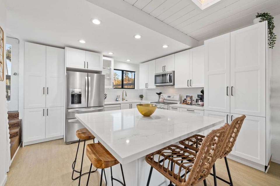 A sleek and contemporary kitchen with bright white cabinetry and stainless steel appliances, centered around a large marble island that serves as a focal point.
