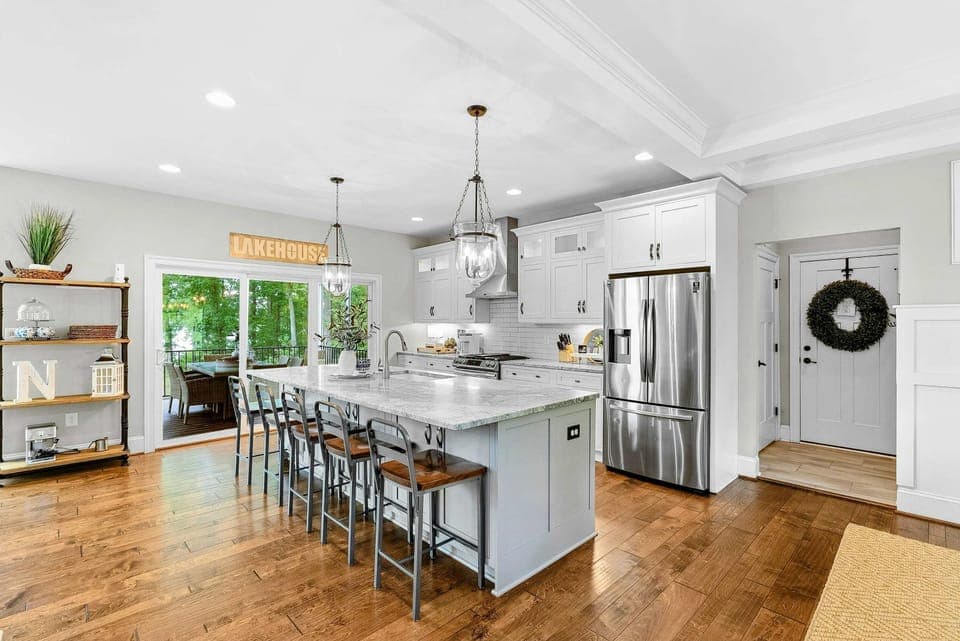 A spacious and modern kitchen with a large marble island, high-end appliances, elegant pendant lighting, and open access to the dining and living areas with views of the backyard.