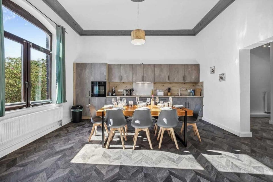 Moderne Einbauküche mit großem Esstisch, stilvollen Stühlen und hohen Fenstern für viel Tageslicht.