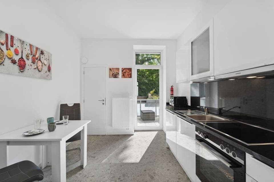 Helle, moderne Küche mit Hochglanzfronten, kompletter Ausstattung und Zugang zum Balkon.