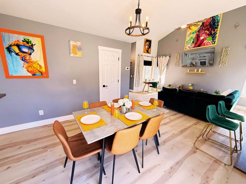 A stylish and inviting dining area with a modern table, sleek leather chairs, vibrant decor, and a chic chandelier—perfect for gatherings and memorable meals
