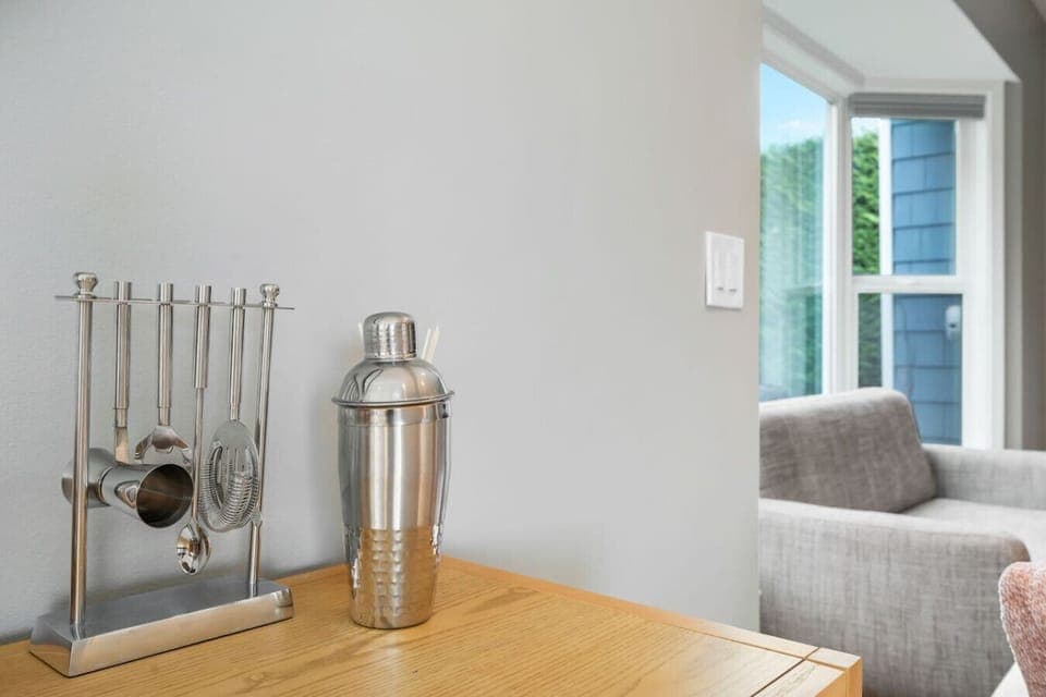 Features a sleek stainless steel cocktail shaker with a textured lower half, accompanied by a matching set of bar tools, including a strainer, spoon, and measuring cup, all neatly arranged on a stand