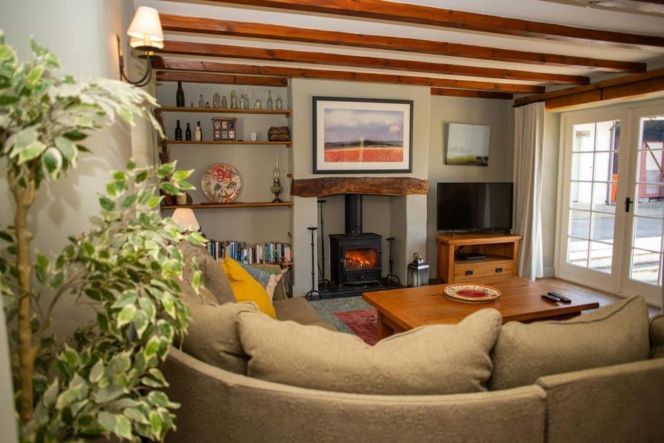 Living room with shelving, wood burner, large corner sofa, TV, coffee table and French doors leading to the patio