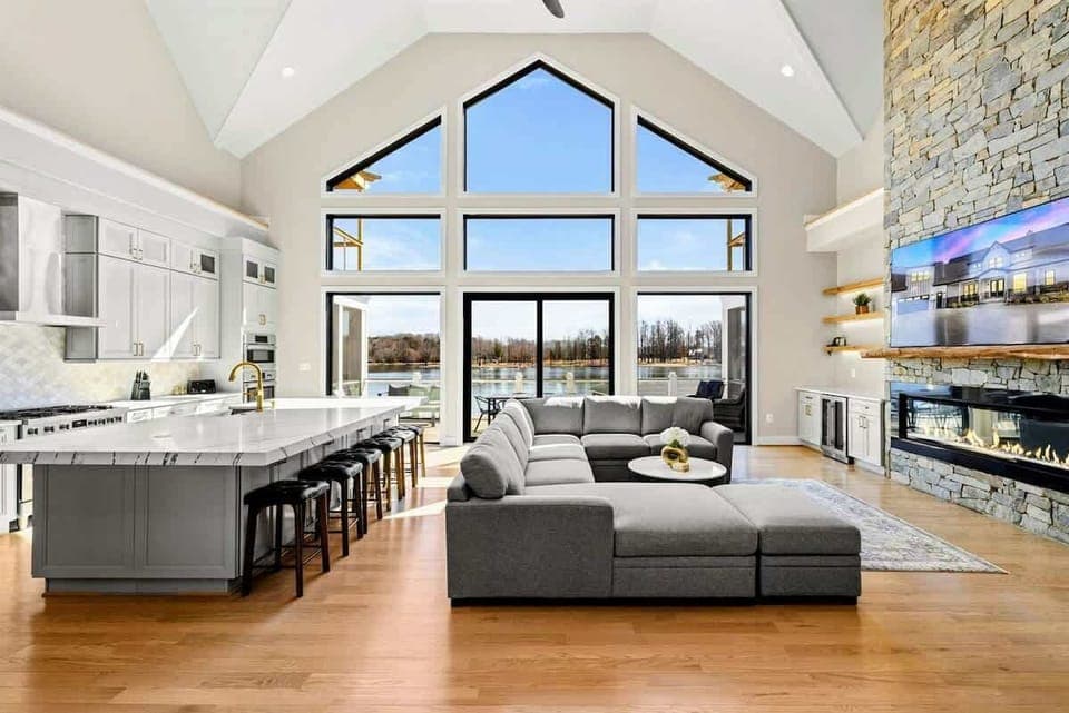Great Room: Bright and sophisticated space featuring vaulted ceilings, expansive windows with stunning lake views, a cozy fireplace, and an open-concept design perfect for relaxing and gathering.