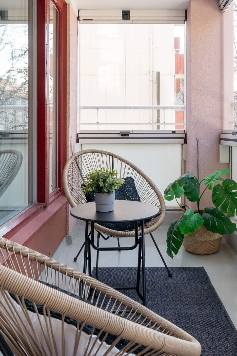 The balcony features comfortable rattan chairs and a small table for outdoor lounging. Enjoy a quiet moment with a view of the surrounding city trees.
