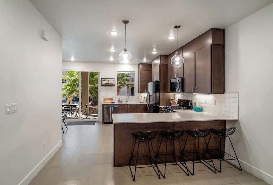 Fully equipped kitchen featuring sleek stainless steel appliances, pendant lighting, and a large island with barstool seating for four.