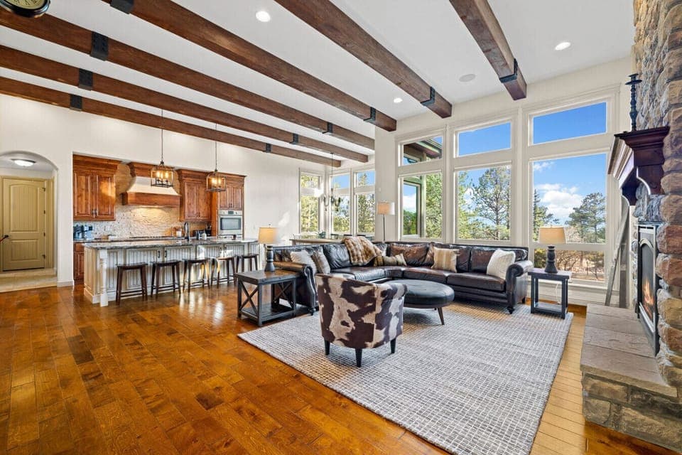 Rustic elegance meets modern comfort—soaring ceilings with exposed beams, a cozy stone fireplace, and panoramic forest views make this open-concept retreat the perfect place to gather and unwind.