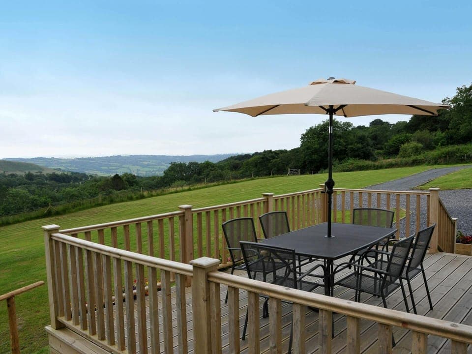 South facing raised decking with six chairs and parasol. Views across fields