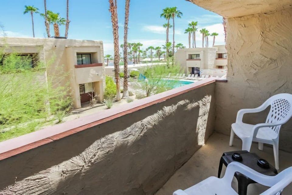 Enjoy the fresh desert air from your private balcony, complete with seating, overlooking lush greenery and the inviting pool area.