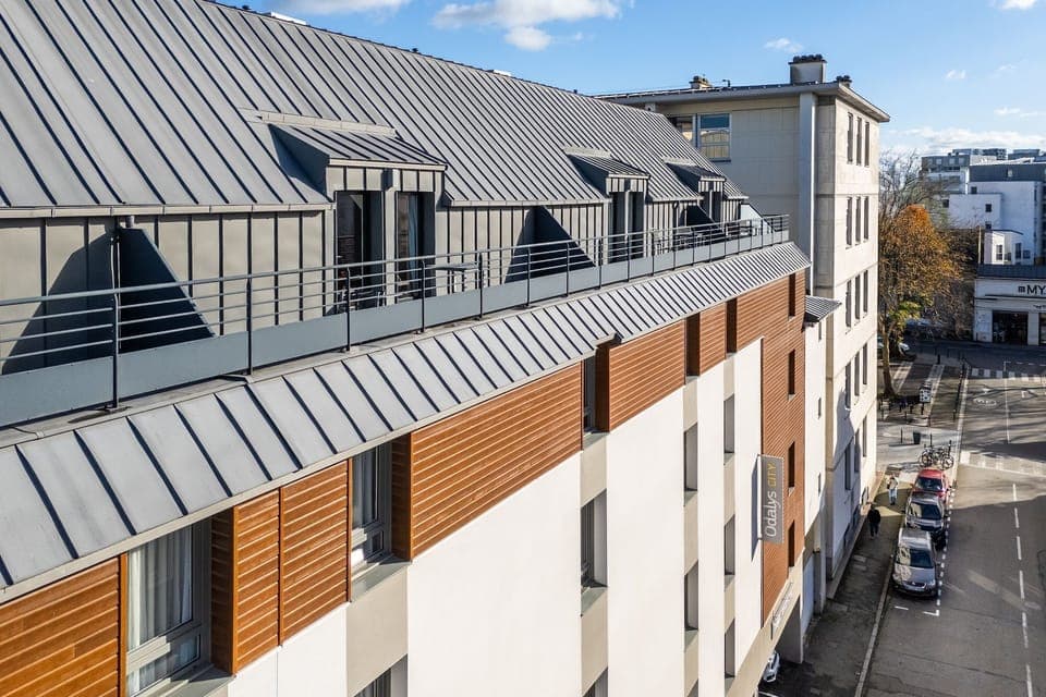 The exterior showcases a contemporary design with a striking combination of sleek metal roofing and warm wooden panels, inviting guests into a modern space right in the heart of Rennes.