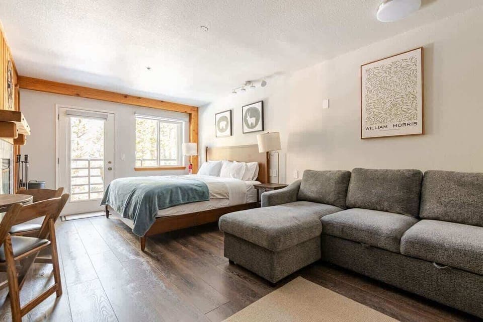 Modern studio with king bed, sofa, table, and balcony.