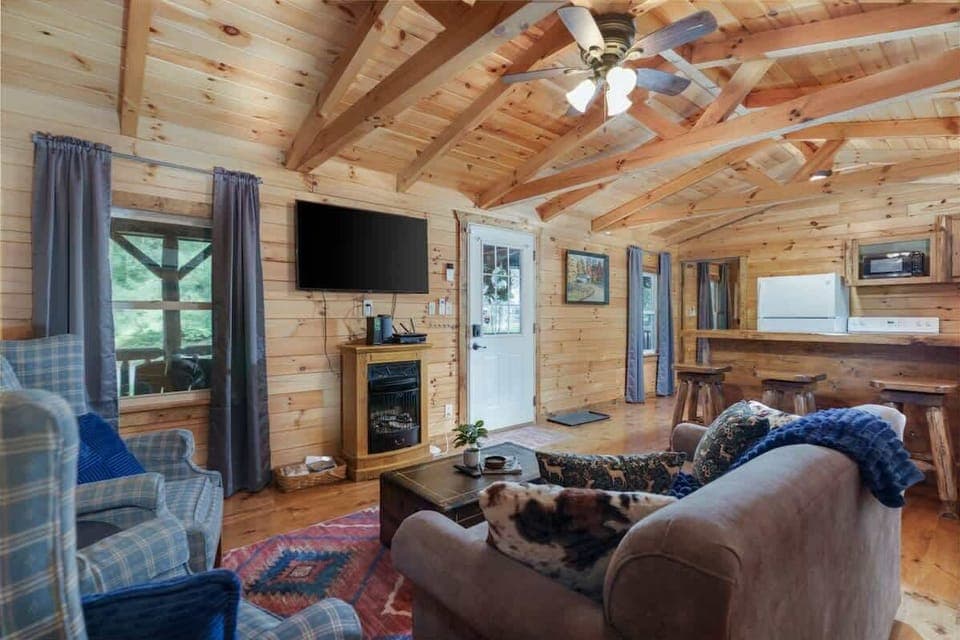 Cozy up in this charming cabin living room ️. Featuring warm wood finishes, a comfy sofa, and an electric fireplace under vaulted ceilings—perfect for movie nights or simply unwinding in rustic comfort 