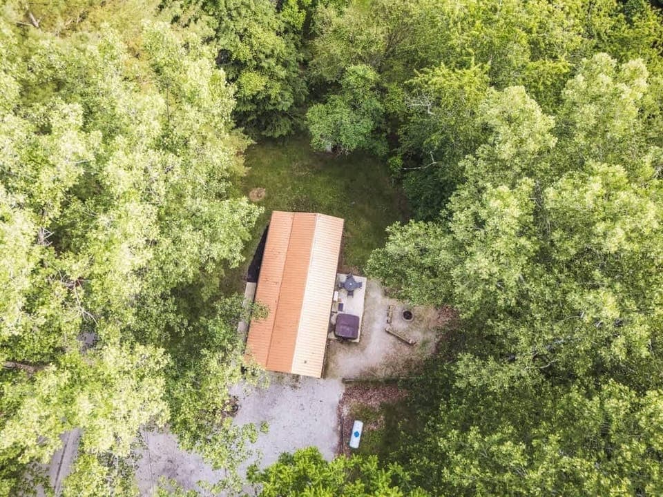 Cozy cabin nestled in lush greenery with a spacious patio featuring a hot tub, fire pit, and outdoor seating—perfect for peaceful nature retreats and relaxing evenings 