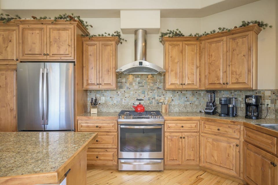 - Modern kitchen with stainless steel appliances and polished stone counters   - Wooden cabinetry and mosaic backsplash add a warm mountain home style   - Fully stocked cooking space offers everything for easy home dining