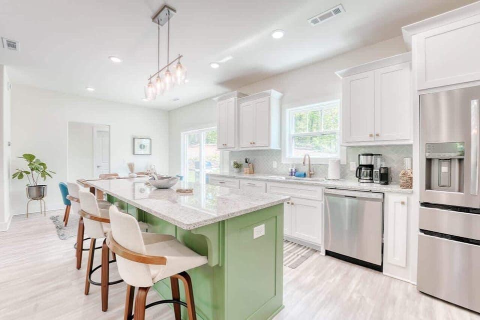 Bright and inviting modern kitchen featuring a large green island with seating, white cabinetry, stainless steel appliances, and ample natural light.