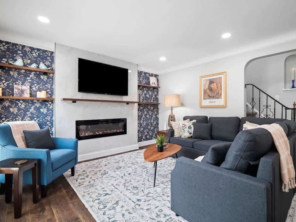 Unwind in this stylish living room featuring a cozy sectional, electric fireplace , and smart TV . Floral accents, modern décor, and soft lighting make it the perfect space to relax after a day out. ️