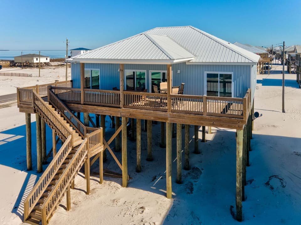 Beachfront retreat elevated on stilts with wraparound deck and sandy shores stretching endlessly beyond.