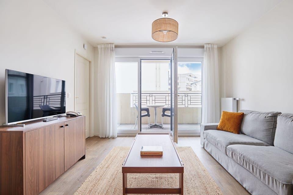 Spacious and bright living room with a flat-screen TV and access to a furnished balcony—perfect for relaxing after exploring Paris.