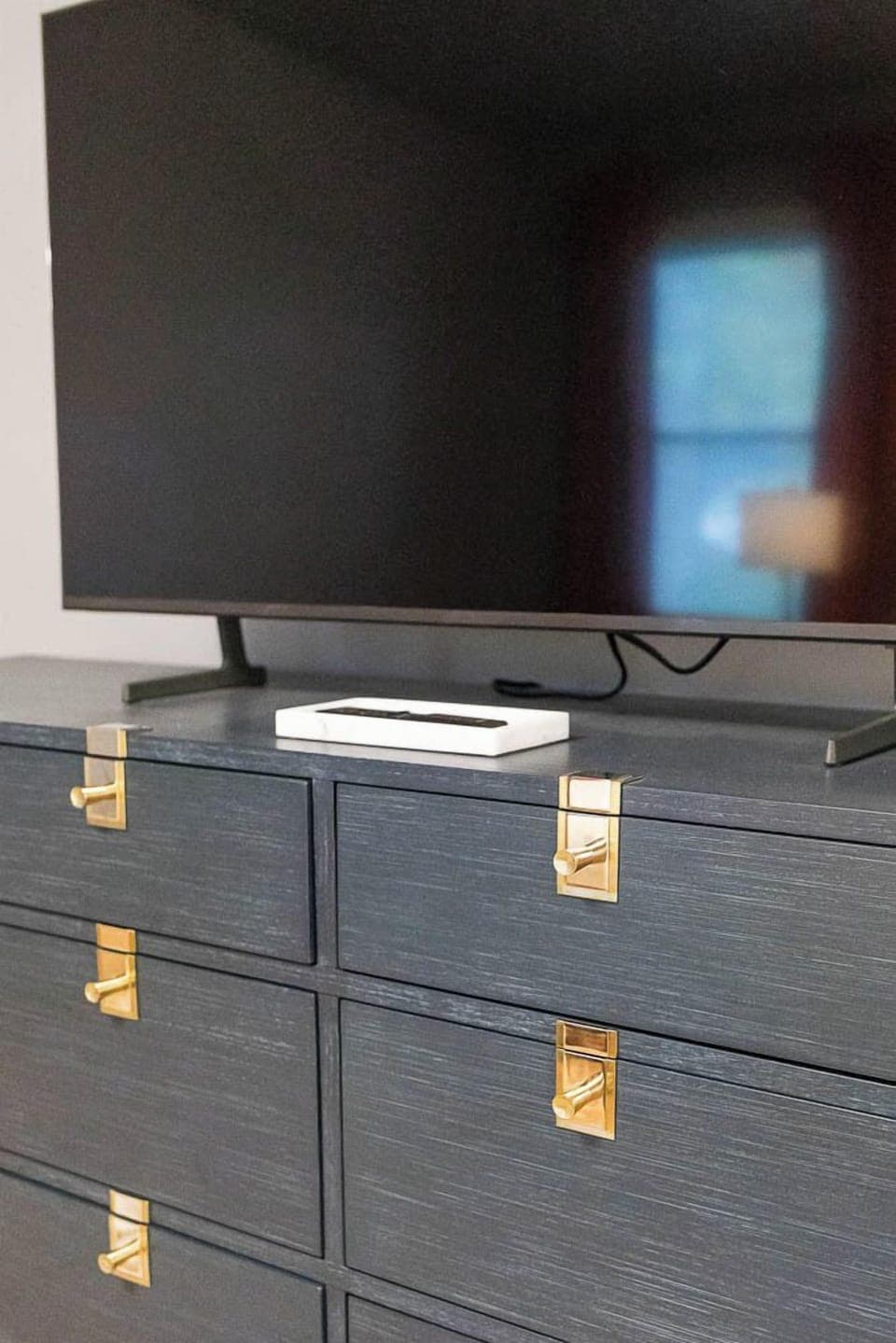 Soft ambient lighting from designer bedside sconces and a statement chandelier creates a serene atmosphere, perfect for unwinding. Matching nightstands and a sleek dresser offer both function and style, while blackout drapes ensure restful sleep.