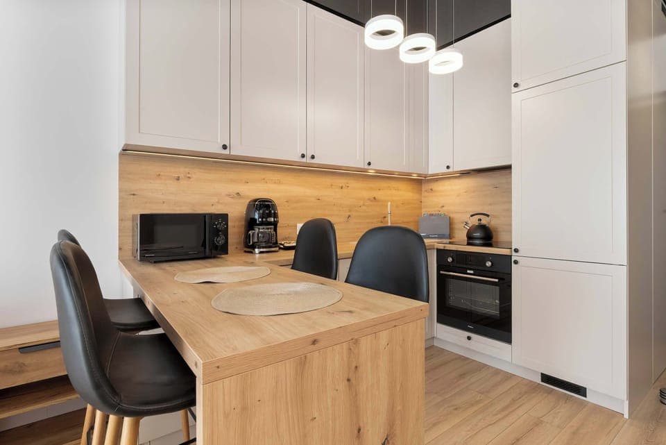 A modern kitchen with white cabinets, black chairs, and a wooden island in the center.